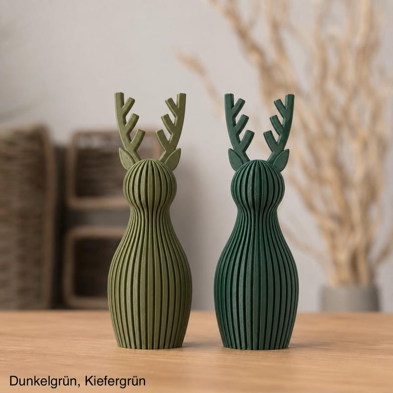 Pu&ograve; includere: Due statuette di cervo in piedi con una texture a coste verticali. Un cervo &egrave; verde oliva chiaro e l'altro &egrave; verde bosco pi&ugrave; scuro. Entrambi presentano corna stilizzate e una forma del corpo arrotondata. Il testo Dunkelgr&uuml;n, Kiefergr&uuml;n &egrave; visibile.