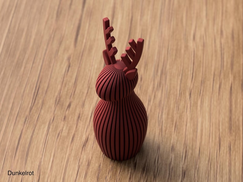 Pu&ograve; includere: Una statuetta di renna color rosso scuro con finitura opaca, costruita con una serie di lamelle verticali parallele. L'oggetto presenta un corpo e una testa arrotondati e bulbosi con due palchi stilizzati e ramificati verso l'alto.