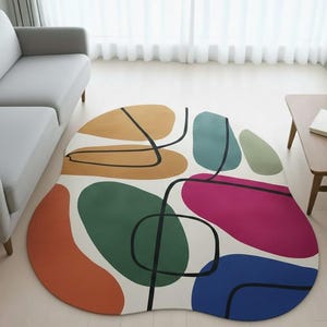 Könnte beinhalten: Abstrakter Teppich mit weißem Hintergrund und bunten, unregelmäßigen Formen. Der Teppich hat orange, grüne, blaue, rosa und beige Formen, die mit schwarzen Linien umrandet sind. Der Teppich befindet sich in einem Wohnzimmer.