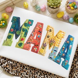May include: A white cushion embroidered with the word "MAMA" in colourful, patterned fabric. The letters feature tropical and summer-themed designs, including flowers, sunglasses, and beach balls. Easter eggs and a succulent plant surround the cushion.