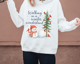 Op de afbeelding: Witte hoodie met een winterthema. Het ontwerp toont een sneeuwpop, een kerstboom en rode vogels. De tekst luidt "Walking in a winter wonderland".