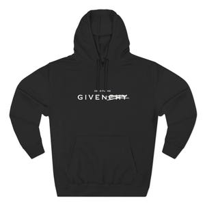 Pode incluir: Moletom preto com texto branco "ZERO FUCKS GIVENCHY", com a palavra "GIVENCHY" riscada. O moletom tem um bolso frontal e um capuz com cordão.