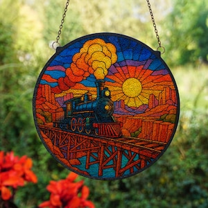 May include: Round stained glass window art featuring a train crossing a wooden bridge against a sunset backdrop. The train is black and blue, with orange and yellow smoke. The background includes a bright yellow sun and red rock formations.
