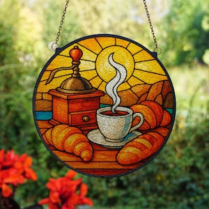 Peut inclure: Vitrail rond représentant une scène de café. On y voit un moulin à café en bois, une tasse de café fumant et des croissants. Le fond montre un soleil et un paysage.