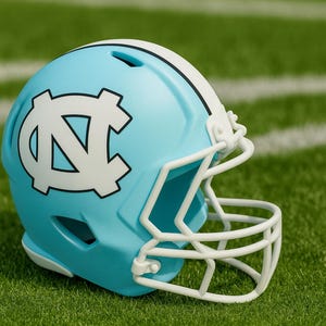 May include: A light blue football helmet with a white facemask and a white stripe down the center. The helmet features a white logo on the side. The helmet is on a green field with white yard lines.