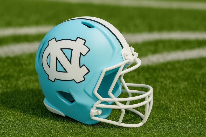 May include: A light blue football helmet with a white facemask and a white stripe down the center. The helmet features a white logo on the side. The helmet is on a green field with white yard lines.