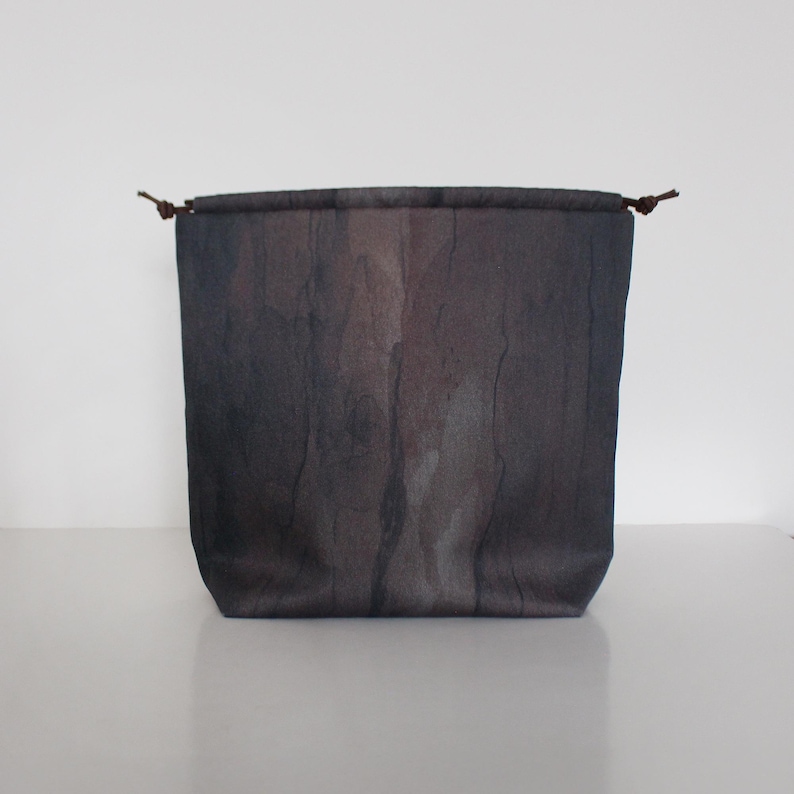 K&ouml;nnte beinhalten: Eine graue Kordeltasche mit einem dezenten Marmormuster. Die Tasche hat braune Lederkordeln.