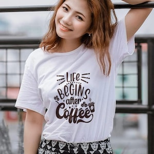 Puede incluir: Camiseta blanca con el texto negro "Life Begins After Coffee". La camiseta tiene cuello redondo y mangas cortas. La persona lleva una falda con estampado en blanco y negro.