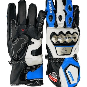 May include: Black, white, and blue motorcycle gloves with the "DUCATI CORSE" logo. The gloves have reinforced knuckles and a wrist strap. The text "SHARP RACER" and "DUCATI" are visible on the gloves.