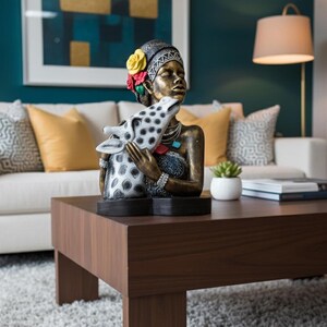May include: A bronze-toned statue of a woman with a floral headpiece, holding a giraffe sculpture. The statue is on a dark brown wooden coffee table. The background includes a white sofa with yellow cushions and a teal wall with framed artwork.
