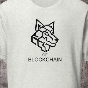 Puede incluir: Camiseta gris claro con un diseño de cabeza de lobo geométrico negro. Debajo del gráfico del lobo, el texto dice "OF BLOCKCHAIN" en negro, fuente sans-serif. La camiseta es de material suave.