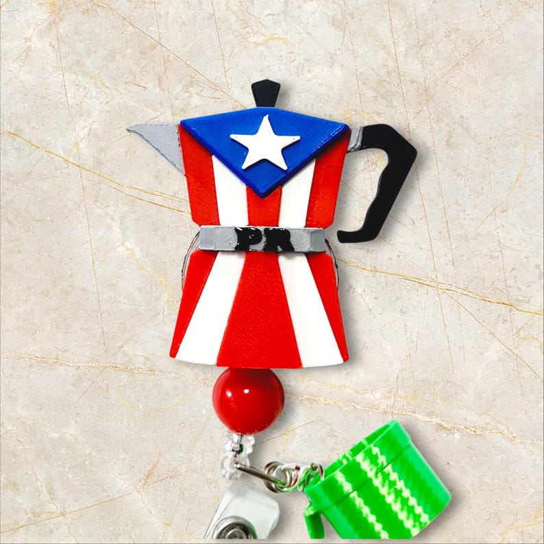 May include: A red, white, and blue Puerto Rican flag-themed coffee maker badge reel. The badge reel has a red ball, a green mug, and a white clip. The coffee maker has the letters "PR" on it.