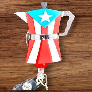 Op de afbeelding: Een novelty badge reel in de vorm van een koffiepot met het ontwerp van de Puerto Ricaanse vlag. De badge reel is rood, wit en blauw, met een ster op de bovenkant. De letters "PR" staan op de riem van de koffiepot.