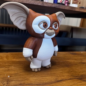 May include: A brown and white figurine of a creature with large pointed ears, round brown eyes, and a small mouth. The figure has a textured surface, a white chest and face patch, and stands on two small feet. It features a smooth, matte finish.