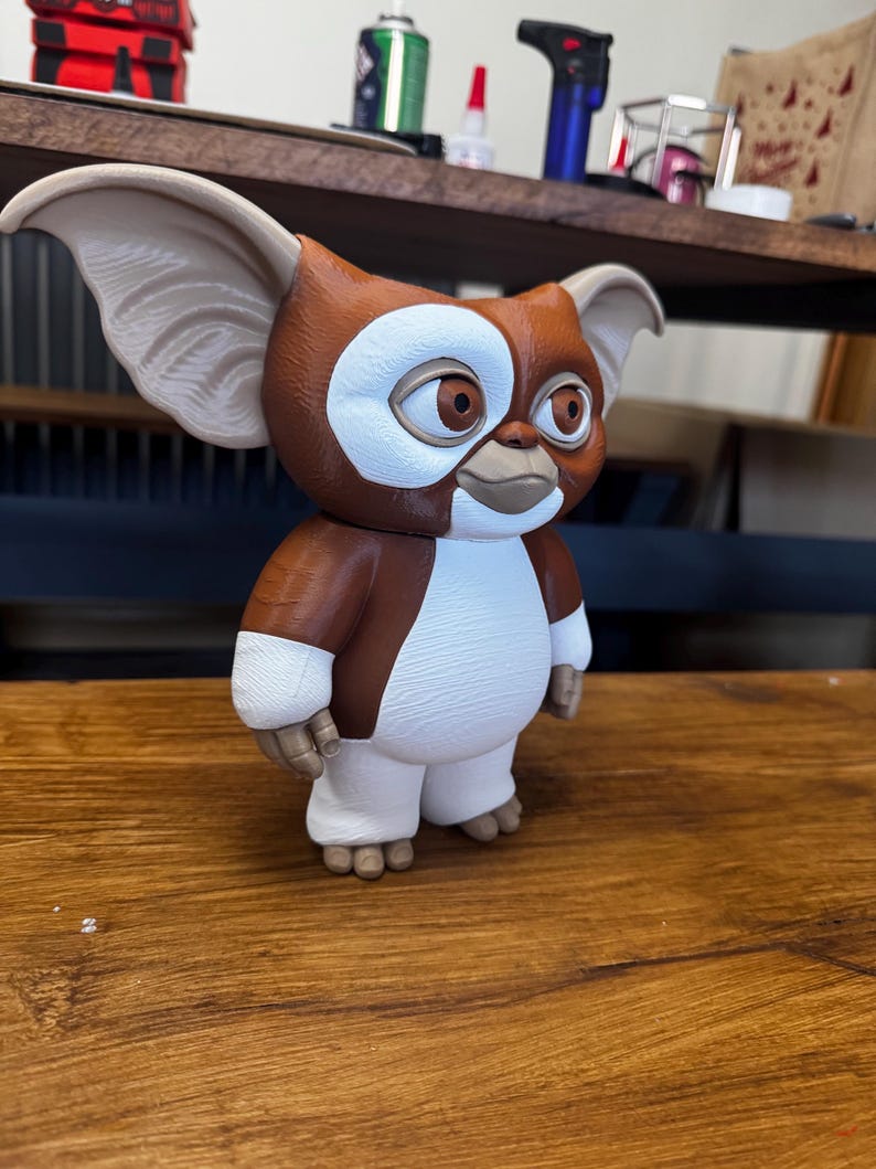May include: A brown and white figurine of a creature with large pointed ears, round brown eyes, and a small mouth. The figure has a textured surface, a white chest and face patch, and stands on two small feet. It features a smooth, matte finish.
