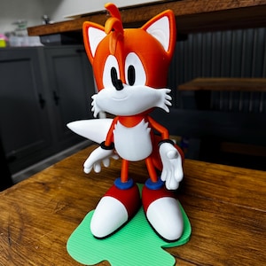 Puede incluir: Figura impresa en 3D de Tails de Sonic the Hedgehog. La figura es naranja y blanca, con detalles rojos y azules. Est&aacute; sobre una base verde. Un personaje popular.