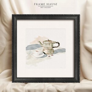 May include: A framed watercolor print featuring a metallic moka pot, a small white cup on a saucer, and two coffee beans. The artwork is enclosed in a black ornate frame with a white mat. The text FRAME HAUSE ART GALLERY appears above the frame.