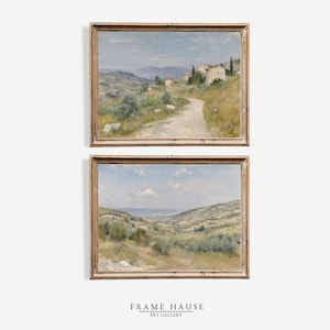 May include: Two framed landscape paintings. The top painting shows a dirt track winding through a hilly landscape with buildings. The bottom painting depicts a valley with trees and a blue sky. Both paintings have a warm colour palette.