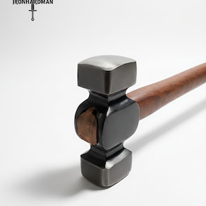 Può includere: Un martello a faccia quadrata con una testa in metallo scuro e un manico in legno. La testa del martello ha una forma distintiva e il manico è di un ricco colore marrone. Il logo "IRONHARDMAN" è visibile in alto a sinistra.