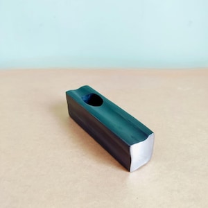 May include: A dark gray, rectangular wooden object with a curved top and a circular hole. The ends are silver. The object is on a light brown surface.
