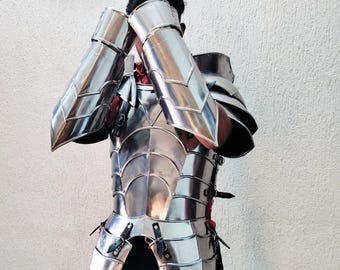 May include: A polished, silver-colored metal armor set. The armor includes a chest plate, shoulder guards, and arm guards. The pieces are connected with straps and buckles. The armor is designed with a layered, segmented construction.