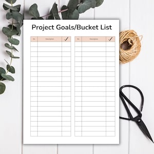 May include: A white Project Goals/Bucket List notepad with a grid of lines for writing. The notepad is on a white wooden surface, with a bundle of twine, scissors, and greenery in the background.