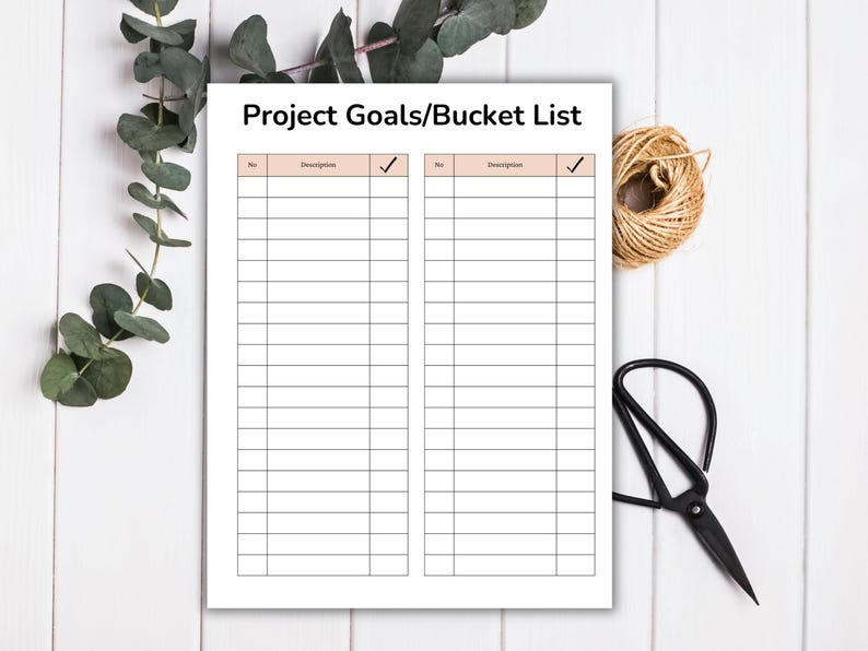 May include: A white Project Goals/Bucket List notepad with a grid of lines for writing. The notepad is on a white wooden surface, with a bundle of twine, scissors, and greenery in the background.