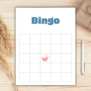 May include: A white Bingo game card with a grid of squares and the word "Bingo" in blue. A pink heart is drawn in the center of the grid. A white pen and a wrapped gift box are on the wooden surface.