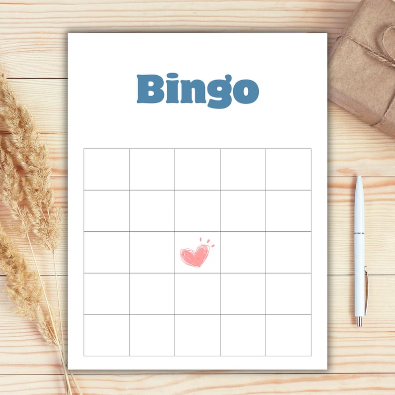 May include: A white Bingo game card with a grid of squares and the word "Bingo" in blue. A pink heart is drawn in the center of the grid. A white pen and a wrapped gift box are on the wooden surface.