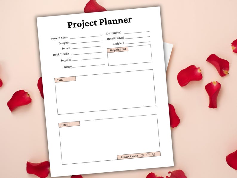 May include: A white Project Planner sheet with sections for pattern details, shopping list, yarn, notes, and project rating. The title "Project Planner" is at the top. Red rose petals are scattered around the planner on a pink background.