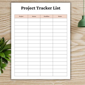 May include: A white Project Tracker List with a grid for tracking projects, status, deadlines, and notes. The title is in bold black font. The background is a light brown wood grain. A green lamp and plant are in the background.