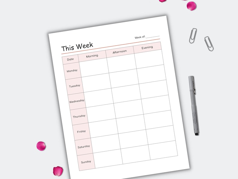 May include: A weekly planner sheet with the title "This Week" at the top. The planner has sections for each day of the week, with columns for morning, afternoon, and evening. A pen and paper clips are next to the planner.