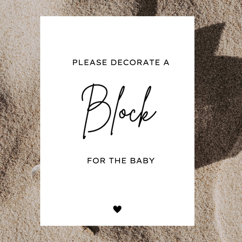 K&ouml;nnte beinhalten: Ein wei&szlig;es rechteckiges Schild mit schwarzem Text: &bdquo;BITTE DEKORIEREN SIE EINEN Block F&Uuml;R DAS BABY&ldquo; mit einem kleinen schwarzen Herz am unteren Rand. Das Schild befindet sich auf einer sandigen Oberfl&auml;che.