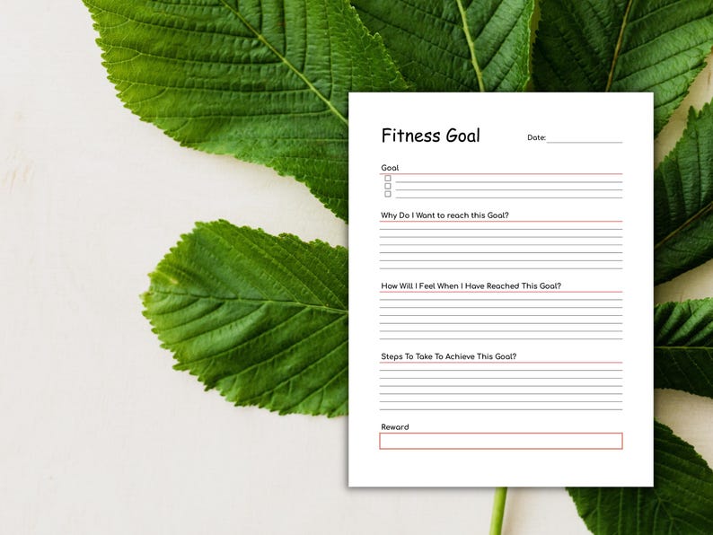 May include: A white fitness goal planner with the title "Fitness Goal" and sections for goals, reasons, feelings, steps, and rewards. The planner is set against a backdrop of green leaves and a white surface.