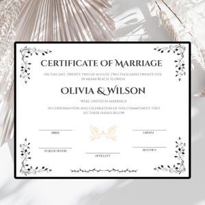 May include: A white marriage certificate with black text and decorative floral corner borders. The document reads Certificate of Marriage, Olivia & Wilson, August 22, 2025, Miami Beach, Florida, with lines for signatures and a central dove illustration.