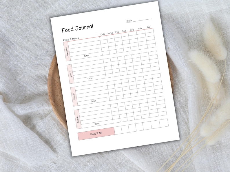 May include: A white Food Journal with pink accents, featuring sections for tracking food intake. The journal includes spaces for recording calories, carbs, fat, sodium, sugar, fiber, and protein. It is designed for daily tracking of breakfast, lunch, dinner, and snacks.