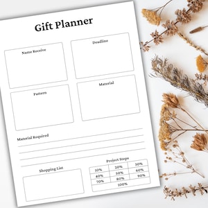 May include: A white Gift Planner sheet with sections for Name, Deadline, Pattern, and Material. It includes a shopping list and project steps with percentage breakdowns. Dried flowers are arranged on the white surface.
