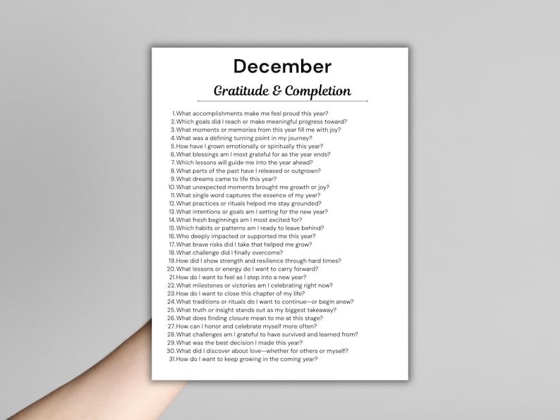 May include: A white paper with the title "December" and "Gratitude & Completion" printed in black. The paper contains a list of 31 questions for reflection, such as "What accomplishments make me feel proud this year?"
