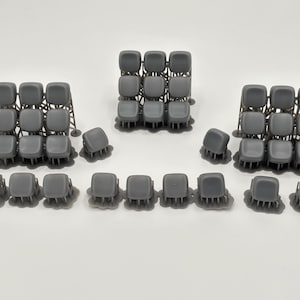 May include: Several gray miniature stadium seating arrangements are displayed against a white background. The sets include rows of seats and individual chairs, likely for model building or crafting projects. The seats are a solid gray color.