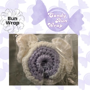 Peut inclure: Un accessoire de coiffure crocheté en forme de chignon, composé d'une spirale centrale lavande entourée d'une bordure blanche à volants, emballé dans un sachet plastique transparent. L'image contient le texte Bun Wrap et Candy Bun Wrap.