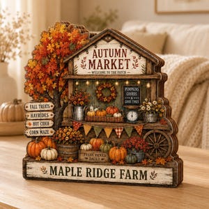 Può includere: Un cartello da tavolo in legno multistrato che raffigura una scena di mercato autunnale con un grande albero arancione, zucche e una ruota di carro. Il cartello presenta le scritte Autumn Market, Welcome to the Patch, Fall Treats, Hayrides, Hot Cider, Corn Maze e Maple Ridge Farm.
