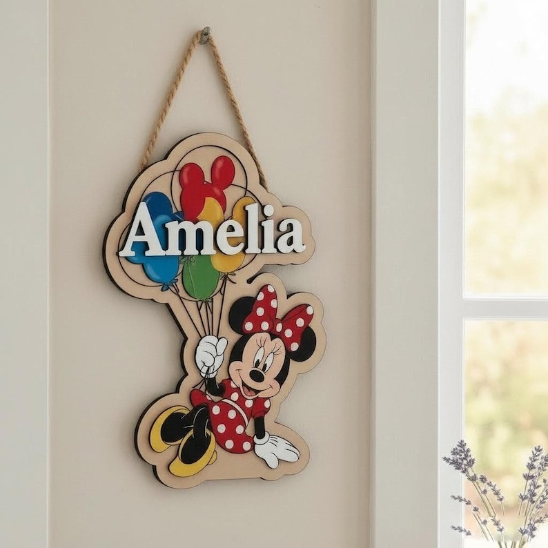 May include: Wooden sign featuring Minnie Mouse holding balloons, with the name "Amelia" in white letters. The sign has a natural wood grain background and a black border, hanging from a rope. The balloons are red, blue, yellow, and green.