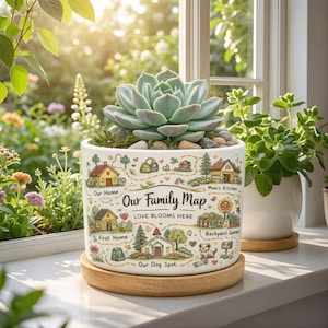May include: A white ceramic planter with a succulent plant, featuring a family map design with houses and text. The planter sits on a wooden coaster, with the text "Our Family Map" and "Love Blooms Here".