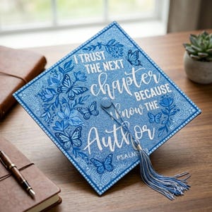 以下が含まれることがあります： 蝶と花の模様が施された青い卒業キャップ。キャップには「I trust the next chapter because I know the Author」と「Psalms 13」の文字が書かれています。青と白のタッセルがキャップからぶら下がっています。