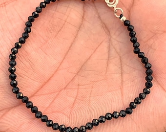 May include: A delicate black beaded bracelet with a silver clasp. The bracelet is composed of small, faceted black beads strung together. The clasp is a simple, silver-toned lobster claw style.