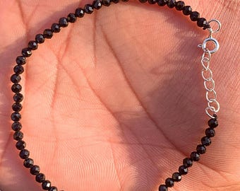 May include: A delicate black beaded bracelet with a silver clasp and extender chain. The bracelet is composed of small, faceted black beads, strung together to form a complete circle. The bracelet is shown on a person's hand.