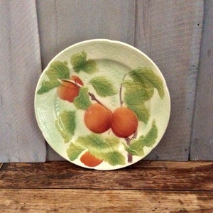 May include: A white ceramic plate with a green and orange design. The plate features a stylized image of a branch with leaves and three orange fruits.