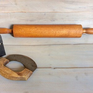 May include: A wooden rolling pin with a natural wood finish and a wooden handle. The rolling pin is on a light wood surface.