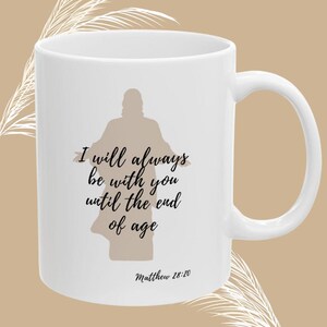 Op de afbeelding: Witte keramische mok met een gebogen handvat, met de tekst "I will always be with you until the end of age" en "Matthew 28:20". De mok heeft ook een silhouet van een persoon met uitgestrekte armen. De onderkant van de mok heeft de tekst "CHRISTIAN MUG MATTHEW SCRIPTURE".