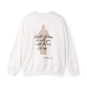 Op de afbeelding: Een witte sweatshirt met lange mouwen. De achterkant toont een silhouet van een figuur met de tekst "I will always be with you until the end of age" en "Matthew 28:20" in een scriptlettertype.
